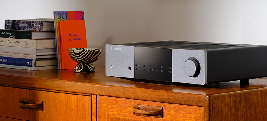 Vue de l’amplificateur Cambridge Audio EXA100 sur un meuble, avec son panneau avant en aluminium et bouton de volume texturé.